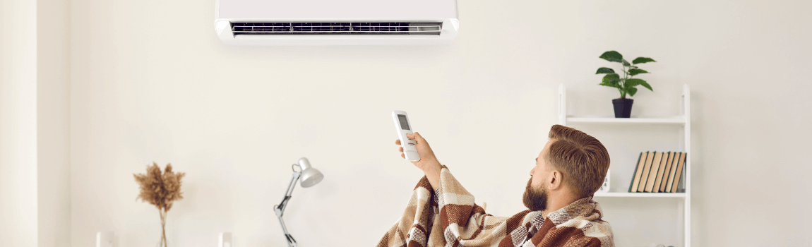 man with blanket on holding remote to heating unit